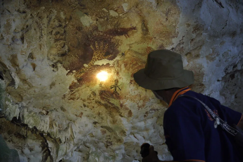 Seorang pemandu lokal menyorot cahaya senter ke lukisan tangan purba di dinding Gua Bloyot. Foto oleh Deta Widyananda.